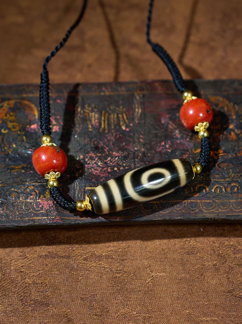 Necklace with red beads and a black and white bead on an old book