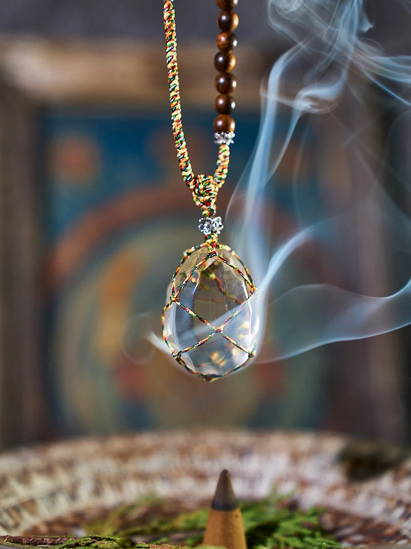Necklace with a teardrop-shaped pendant emitting smoke against a blurred background