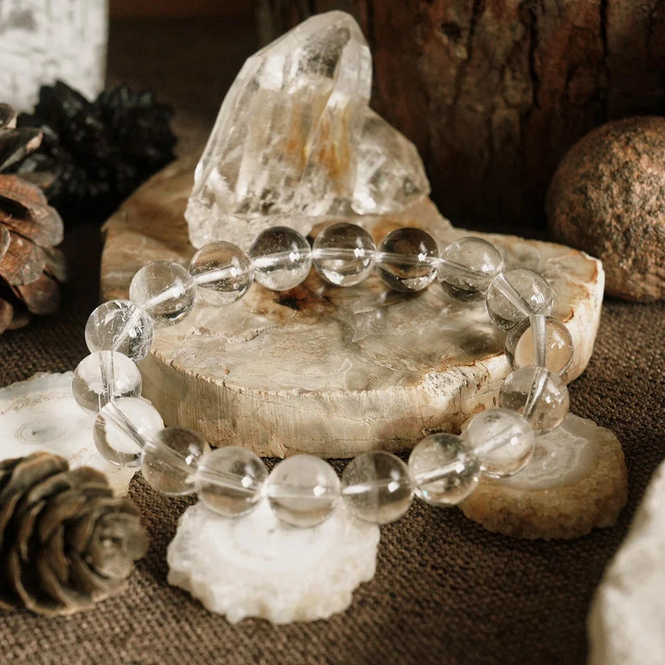 Clear beaded bracelet on a wooden surface with crystals and pinecones
