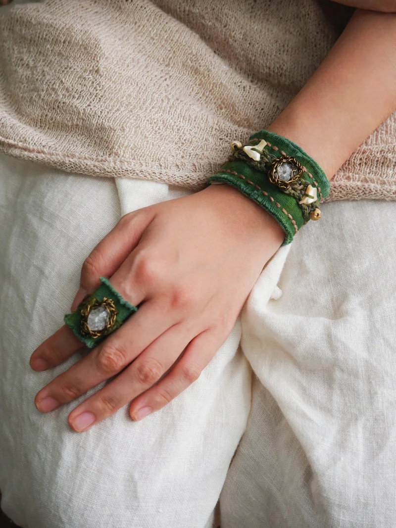 Hand wearing a green bracelet and ring on a neutral background